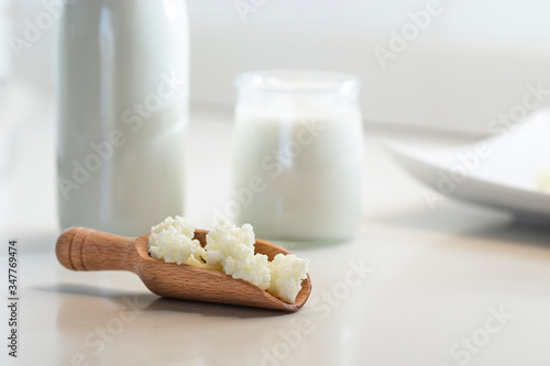 Milk kefir grains in wooden spoon with a glass of kefir in the back