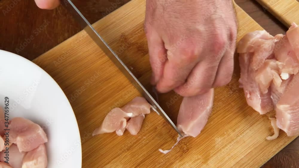 Man s hands with knife slices delicate chicken fillet on cut board. Man s hands with knife slices delicate chicken fillet on cut board.