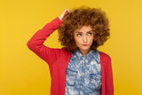 Deep in thoughts. Portrait of pensive confused woman with curly hair in casual outfit scratching head, wondering and having doubts, pondering idea. indoor studio shot isolated on yellow background