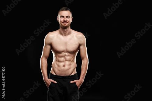 Strong athletic man - athlete fitness model showing his perfect body isolated on black background with copyspace. Ectomorph bodybuilder with perfect abs, shoulders, biceps, triceps and chest.
