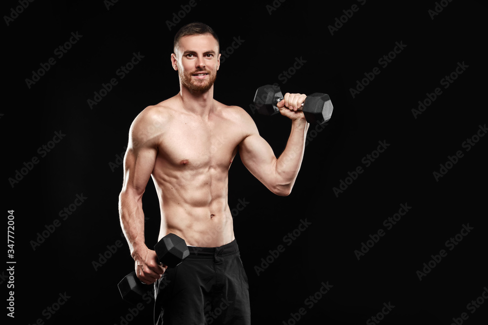 Strong athletic man - crossfit athlete fitness model showing his perfect body isolated on black background with copyspace. Ectomorph bodybuilder holding a black new dumbbell in his hands.
