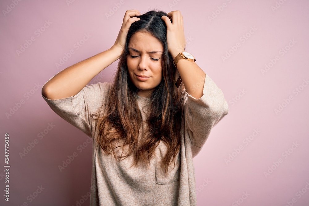 Young beautiful brunette woman wearing casual sweater standing over pink background suffering from headache desperate and stressed because pain and migraine. Hands on head.