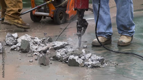 A Worker places a jackhammer tip on cement and starts chipping away the cement. photo