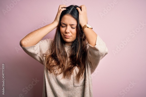 Young beautiful brunette woman wearing casual sweater standing over pink background suffering from headache desperate and stressed because pain and migraine. Hands on head.