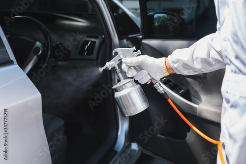 Close up hand of specialist cleaner wearing personal protective equipment PPE using chemical alcohol spray cleaning inside car to disinfect and decontaminate coronavirus covid-19