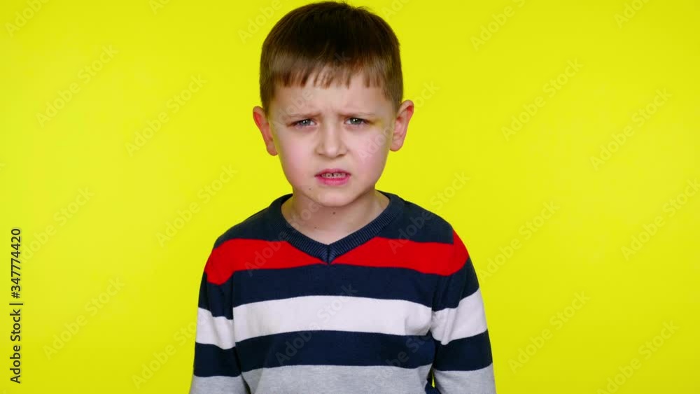 Confused little boy growls at the camera on a yellow background with copy space. Little child in a colorful sweater. Place for text or product. 4K slowmotion footage Confused little boy growls at the camera on a yellow background with copy space. Little child in a colorful sweater. Place for text or product. 4K slowmotion footage