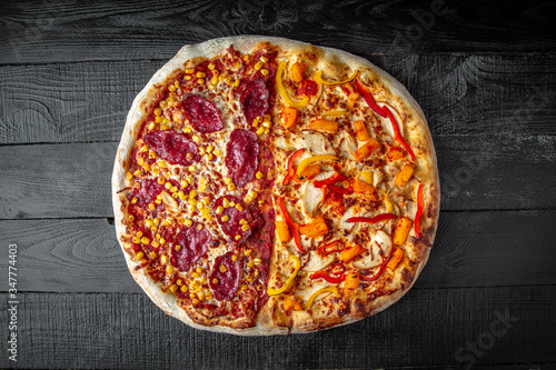 Tasty hot italian big two-in-one pizza with chicken, pineapple and pepperoni and corn on black wooden table. Pizzeria menu. Concept poster for Restaurants or pizzerias