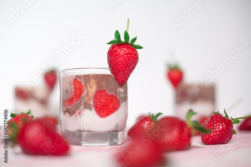light strawberry dessert in a glass on a light background with fresh strawberries and cream and chocolate cream layers