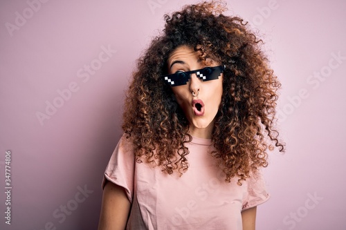 Young beautiful woman with curly hair and piercing wearing funny thug life sunglasses afraid and shocked with surprise expression  fear and excited face.