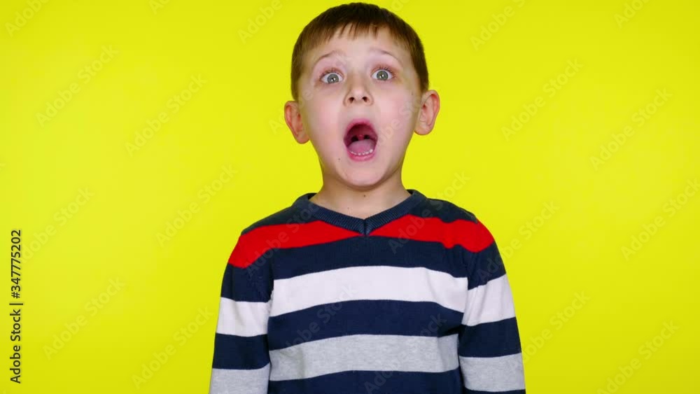 Little kid boy in a colorful sweater is surprised on a yellow background with copy space. Place for text or product. 4K slowmotion footage