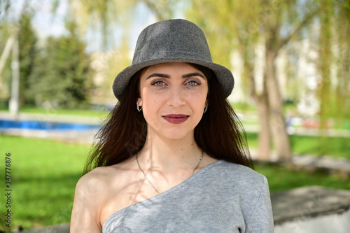 Model posing in spring park outdoors with a smile. Close-up portrait of a cute young caucasian brunette girl in a gray dress and black hat in various poses.