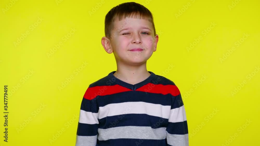 Little child boy in a multi-colored sweater smiles and blinks an eye on a yellow background with copy space. Place for text or product. 4K slowmotion footage Little child boy in a multi-colored sweater smiles and blinks an eye on a yellow background with copy space. Place for text or product. 4K slowmotion footage