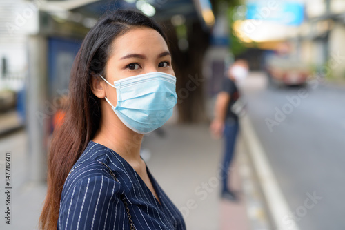 Face of young Asian businesswoman with mask for protection from corona virus outbreak waiting at the bus stop