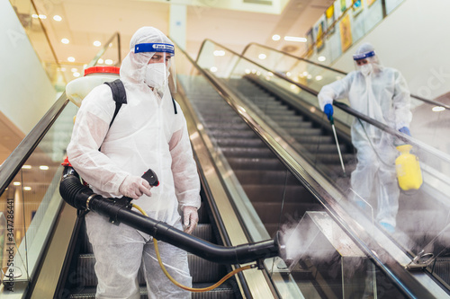 Professional workers in hazmat suits disinfecting indoor of mall, pandemic health risk, coronavirus photo