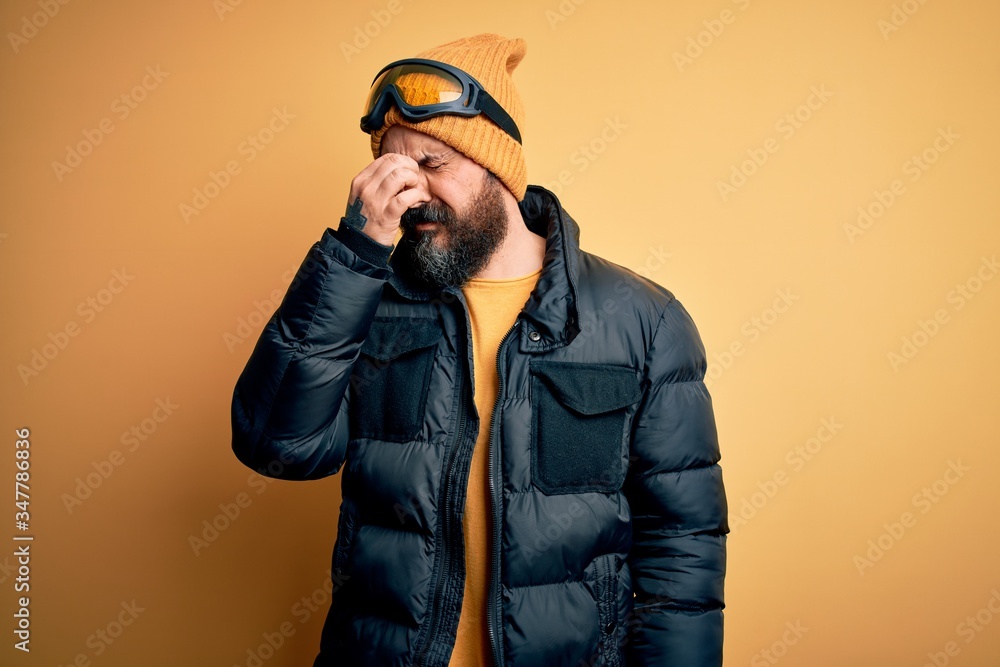 Handsome skier bald man with beard skiing wearing snow sportswear and ski goggles tired rubbing nose and eyes feeling fatigue and headache. Stress and frustration concept. Handsome skier bald man with beard skiing wearing snow sportswear and ski goggles tired rubbing nose and eyes feeling fatigue and headache. Stress and frustration concept.