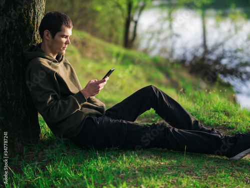 relaxed young man with a smartphone in his hand at sunset by the river Bank . Lifestyle, harmony