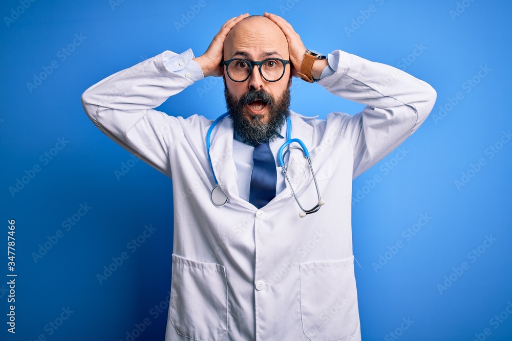 Handsome bald doctor man with beard wearing glasses and stethoscope over blue background Crazy and scared with hands on head, afraid and surprised of shock with open mouth Handsome bald doctor man with beard wearing glasses and stethoscope over blue background Crazy and scared with hands on head, afraid and surprised of shock with open mouth