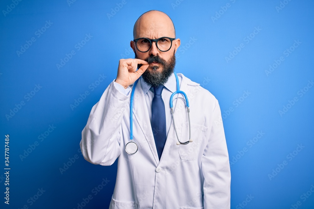Handsome bald doctor man with beard wearing glasses and stethoscope over blue background mouth and lips shut as zip with fingers. Secret and silent, taboo talking Handsome bald doctor man with beard wearing glasses and stethoscope over blue background mouth and lips shut as zip with fingers. Secret and silent, taboo talking