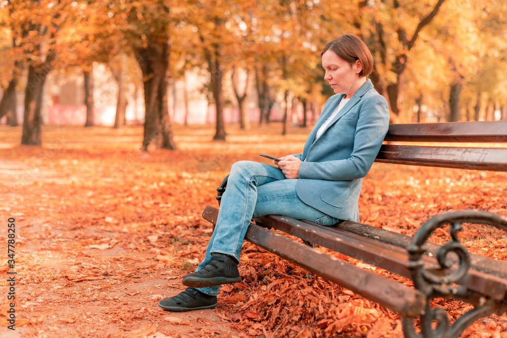 Woman typing text on mobile phone on autumn park bench Woman typing text on mobile phone on autumn park bench