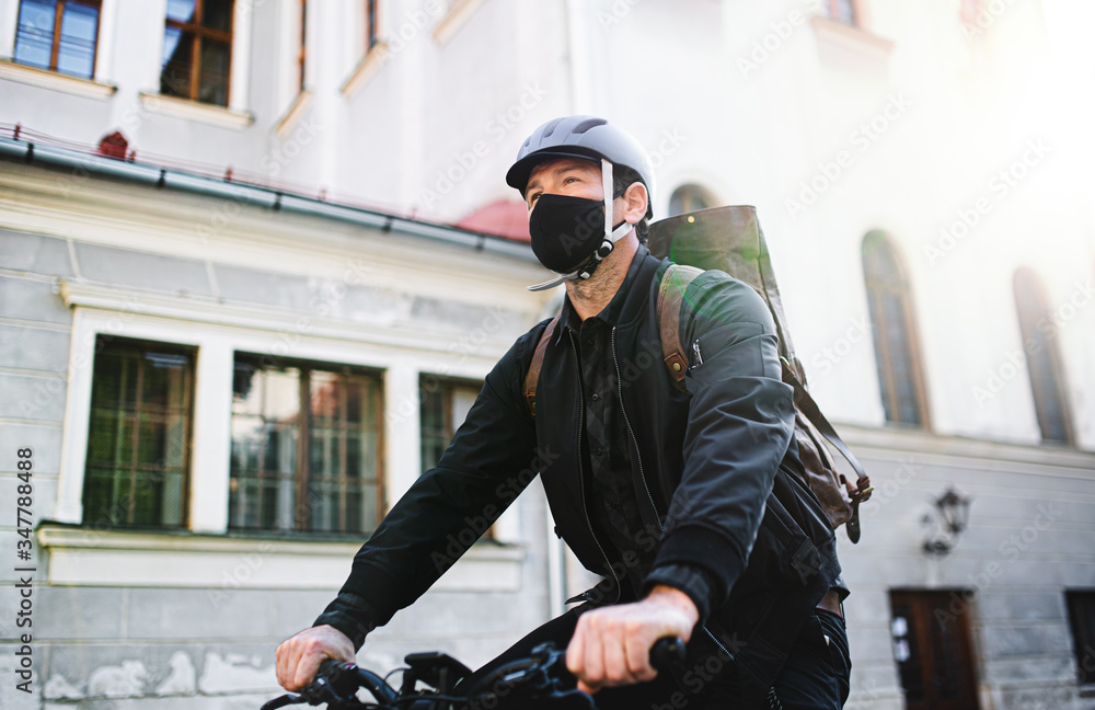 Delivery man courier with face mask and bicycle cycling in town. Delivery man courier with face mask and bicycle cycling in town.