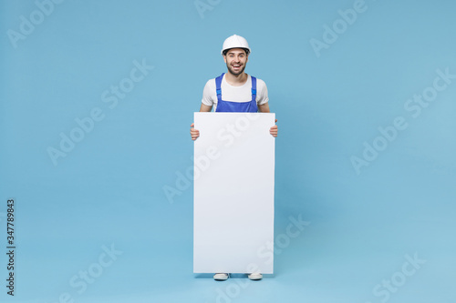 Cheerful man in coveralls hardhat hold white empty blank billboard with place for text image isolated on pastel blue background. Instruments accessories renovation apartment room. Repair home concept. photo