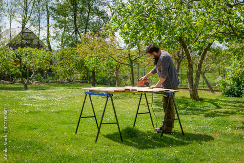 Mid adult caucasian man in the garden sanding wooden planks. DIY home improvement, restoration, carpentry concept.