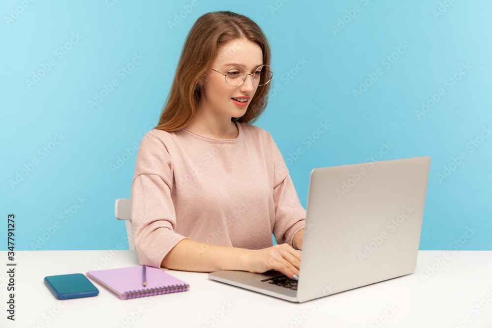 Smart woman in nerd eyeglasses typing on laptop, working with clever diligent expression in office. Student studying, doing online internet course. indoor studio shot isolated on blue background Smart woman in nerd eyeglasses typing on laptop, working with clever diligent expression in office. Student studying, doing online internet course. indoor studio shot isolated on blue background