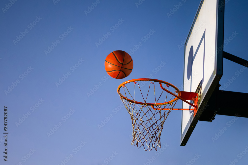Street basketball ball falling into the hoop. Close up of orange ball above the hoop net with blue sky in the background. Concept of success, scoring points and winning. Copy space