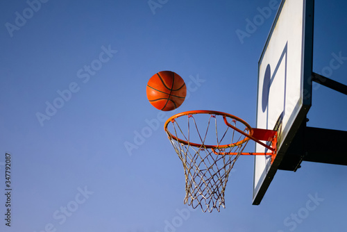 Street basketball ball falling into the hoop. Close up of orange ball above the hoop net with blue sky in the background. Concept of success, scoring points and winning. Copy space