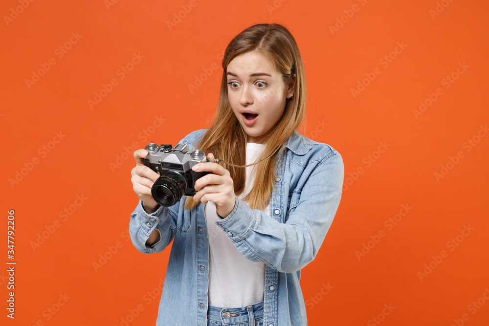 Shocked young woman girl in casual denim clothes posing isolated on orange background studio portrait. People sincere emotions lifestyle concept. Mock up copy space. Hold retro vintage photo camera.