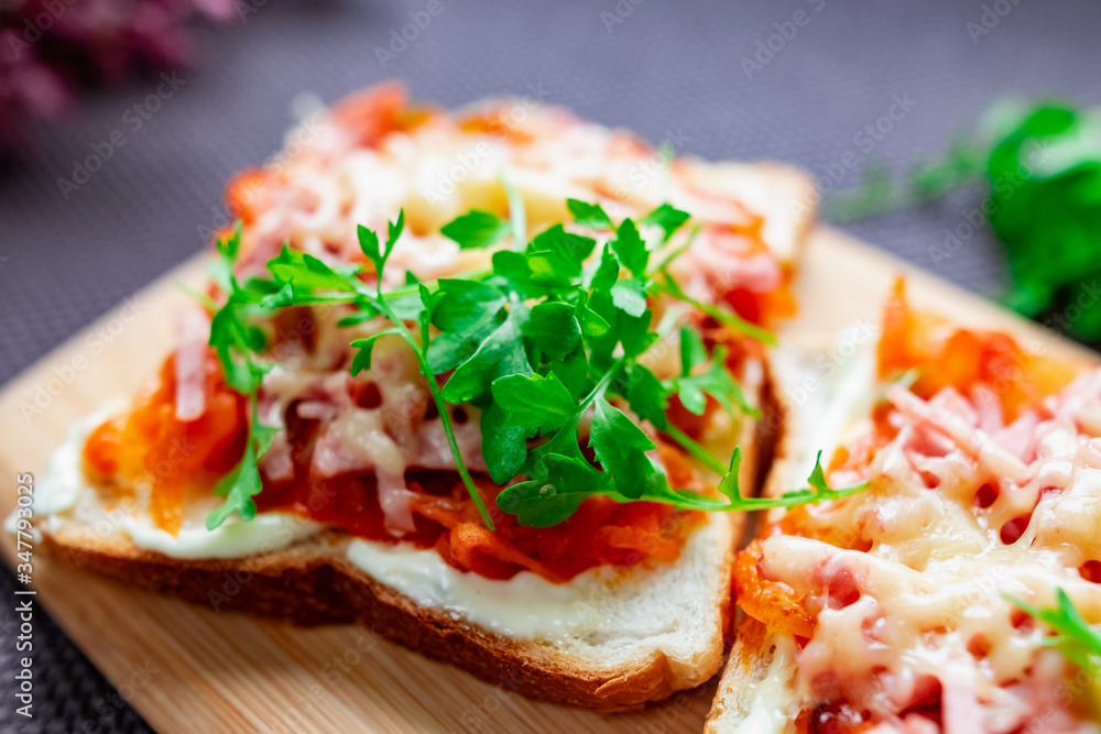 Baked hot sandwiches on white bread with fried vegetables in tomato sauce, Servelat straws, melted cheese and green watercress on a wooden Board Baked hot sandwiches on white bread with fried vegetables in tomato sauce, Servelat straws, melted cheese and green watercress on a wooden Board