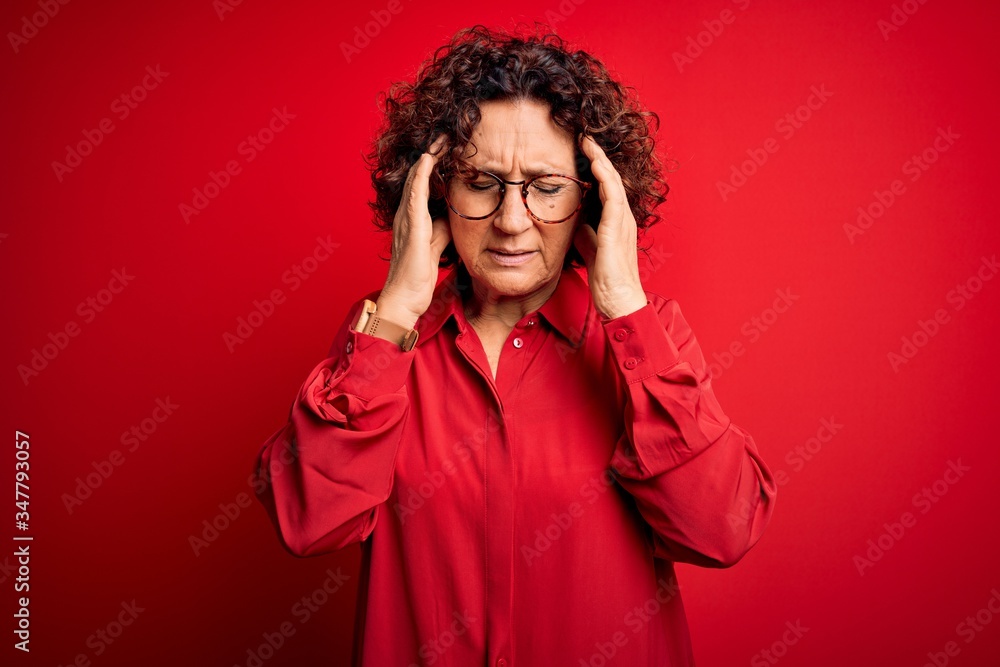 Middle age beautiful curly hair woman wearing casual shirt and glasses over red background with hand on headache because stress. Suffering migraine. Middle age beautiful curly hair woman wearing casual shirt and glasses over red background with hand on headache because stress. Suffering migraine.