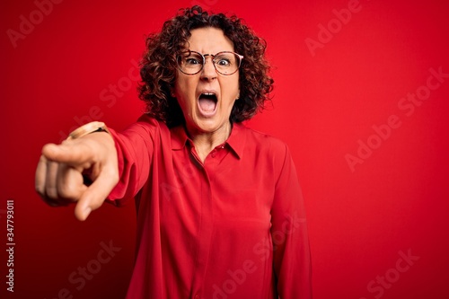 Middle age beautiful curly hair woman wearing casual shirt and glasses over red background pointing displeased and frustrated to the camera, angry and furious with you