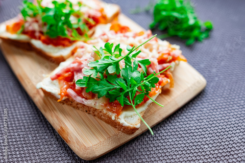 Baked hot sandwiches on white bread with fried vegetables in tomato sauce, Servelat straws, melted cheese and green watercress on a wooden Board