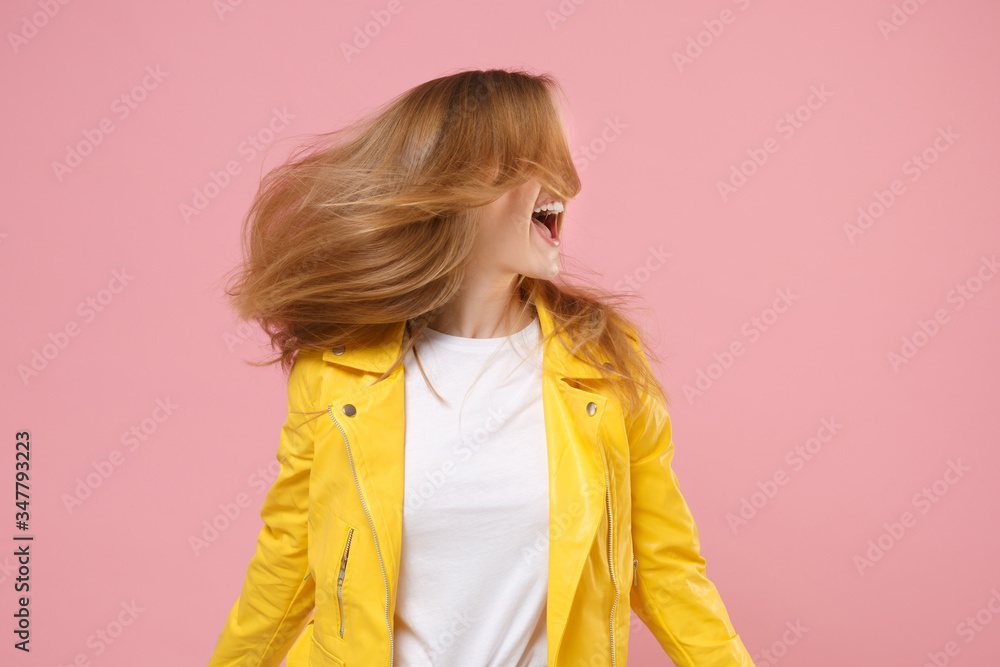Excited young woman girl in yellow leather jacket posing isolated on pastel pink background in studio. People lifestyle concept. Mock up copy space. Having fun jumping with flowing hair looking aside. Excited young woman girl in yellow leather jacket posing isolated on pastel pink background in studio. People lifestyle concept. Mock up copy space. Having fun jumping with flowing hair looking aside.