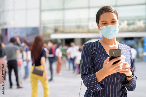 Wallpaper Mural Young Asian businesswoman with mask using phone while having coffee on the go as the new normal during covid-19 Torontodigital.ca
