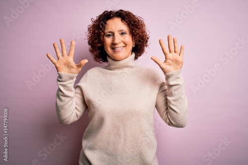 Middle age beautiful curly hair woman wearing casual turtleneck sweater over pink background showing and pointing up with fingers number ten while smiling confident and happy.