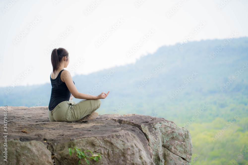 young woman doing yoga exercise on the top of the mountain 