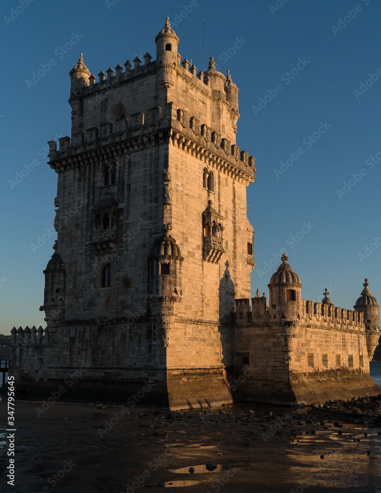 Lisbon, view of the Belem Tower wall on the sunset side, the Tagus River is at low tide and the rocky beach is without water