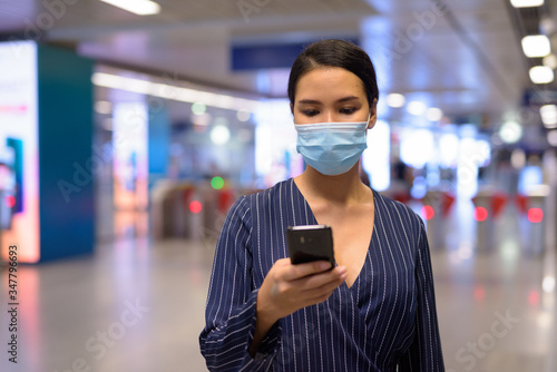Young Asian businesswoman with mask using phone at the subway train station