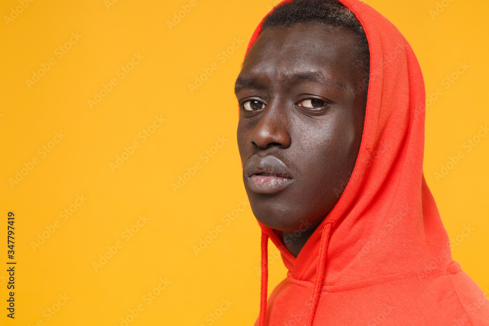 Side view of young african american man guy in red streetwear hoodie with hood on head posing isolated on yellow background in studio. People lifestyle concept. Mock up copy space. Looking camera. Side view of young african american man guy in red streetwear hoodie with hood on head posing isolated on yellow background in studio. People lifestyle concept. Mock up copy space. Looking camera.