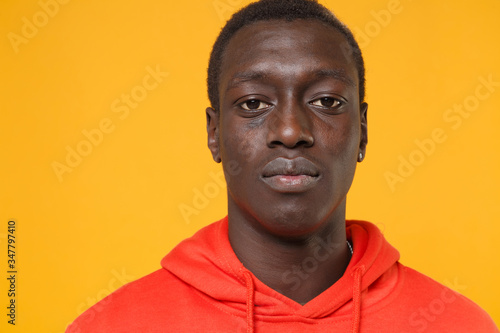 Close up of young african american man guy in red streetwear hoodie posing isolated on yellow background studio portrait. People sincere emotions lifestyle concept. Mock up copy space. Looking camera.