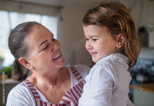 Small girl with senior grandmother in kitchen indoors at home.