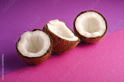 Coconut fruits in row on violet and purple plain background, abstract food tropical concept, angle view