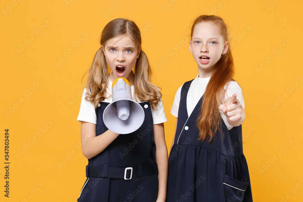 Two fun girls 12-13 years old in white t-shirt blue school uniform dresse scream in megaphone isolated on yellow background children studio portrait Childhood kids education concept Mock up copy space Two fun girls 12-13 years old in white t-shirt blue school uniform dresse scream in megaphone isolated on yellow background children studio portrait Childhood kids education concept Mock up copy space