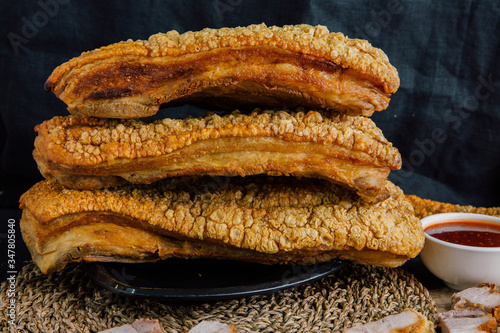 Large crispy pork on a black plate, cut into slices on a wooden chopping board with spicy sauce on a wooden table