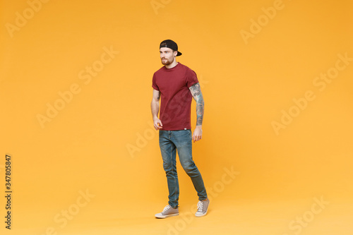 Handsome young tattooed man guy in casual t-shirt black cap posing isolated on yellow wall background studio portrait. People sincere emotions lifestyle concept. Mock up copy space. Looking aside.