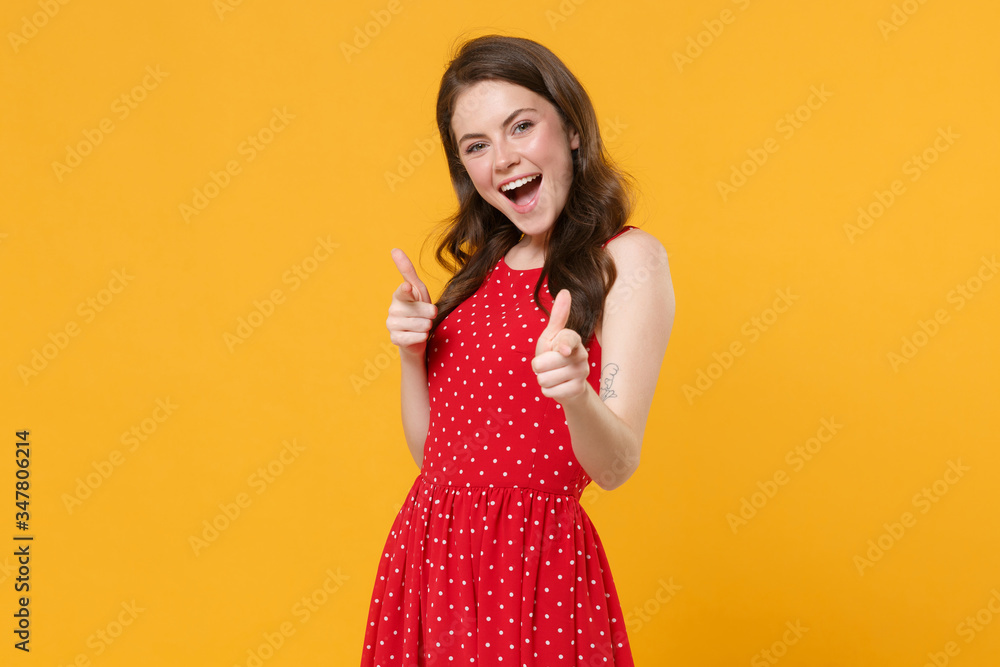 Cheerful young brunette woman girl in red summer dress posing isolated on yellow background studio portrait. People emotions lifestyle concept. Mock up copy space. Pointing index fingers on camera. Cheerful young brunette woman girl in red summer dress posing isolated on yellow background studio portrait. People emotions lifestyle concept. Mock up copy space. Pointing index fingers on camera.