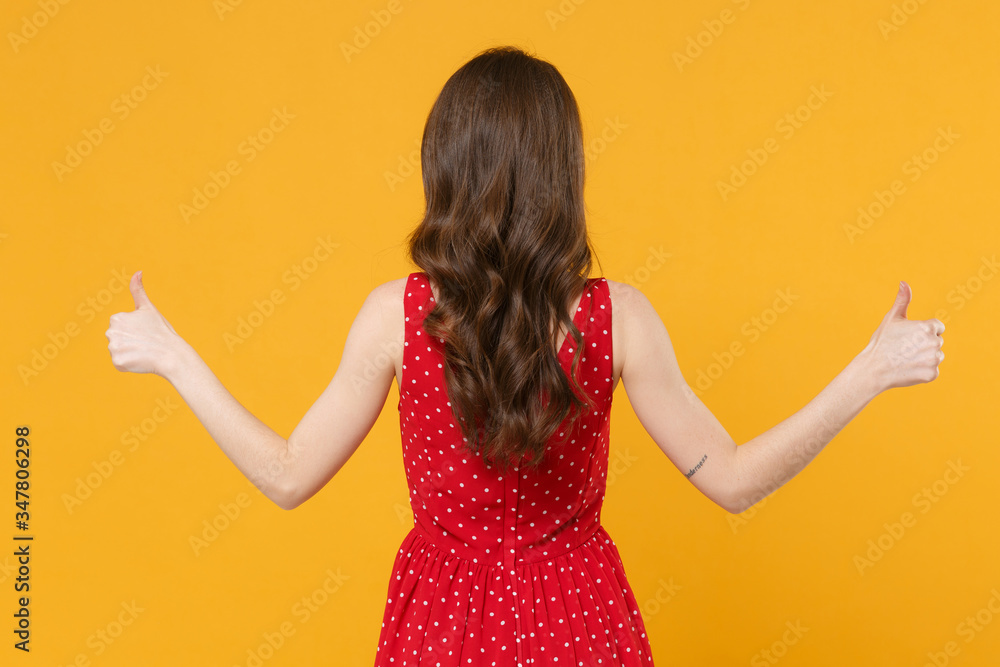 Back rear view of young brunette woman girl in red summer dress posing isolated on yellow background studio portrait. People sincere emotions lifestyle concept. Mock up copy space. Showing thumbs up. Back rear view of young brunette woman girl in red summer dress posing isolated on yellow background studio portrait. People sincere emotions lifestyle concept. Mock up copy space. Showing thumbs up.