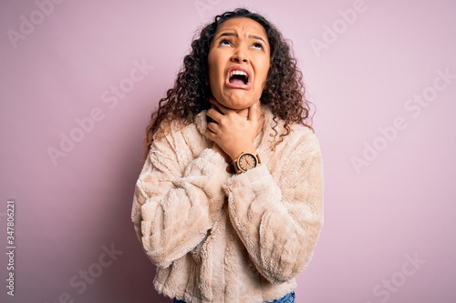 Young beautiful woman with curly hair wearing casual sweater standing over pink background shouting suffocate because painful strangle. Health problem. Asphyxiate and suicide concept.